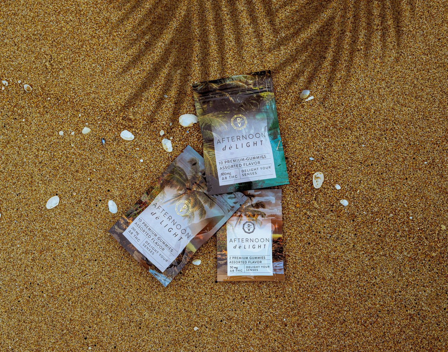 Afternoon deLIGHT ∆8 Gummies three assorted flavored packs displayed on a textured sandy surface with small shells.