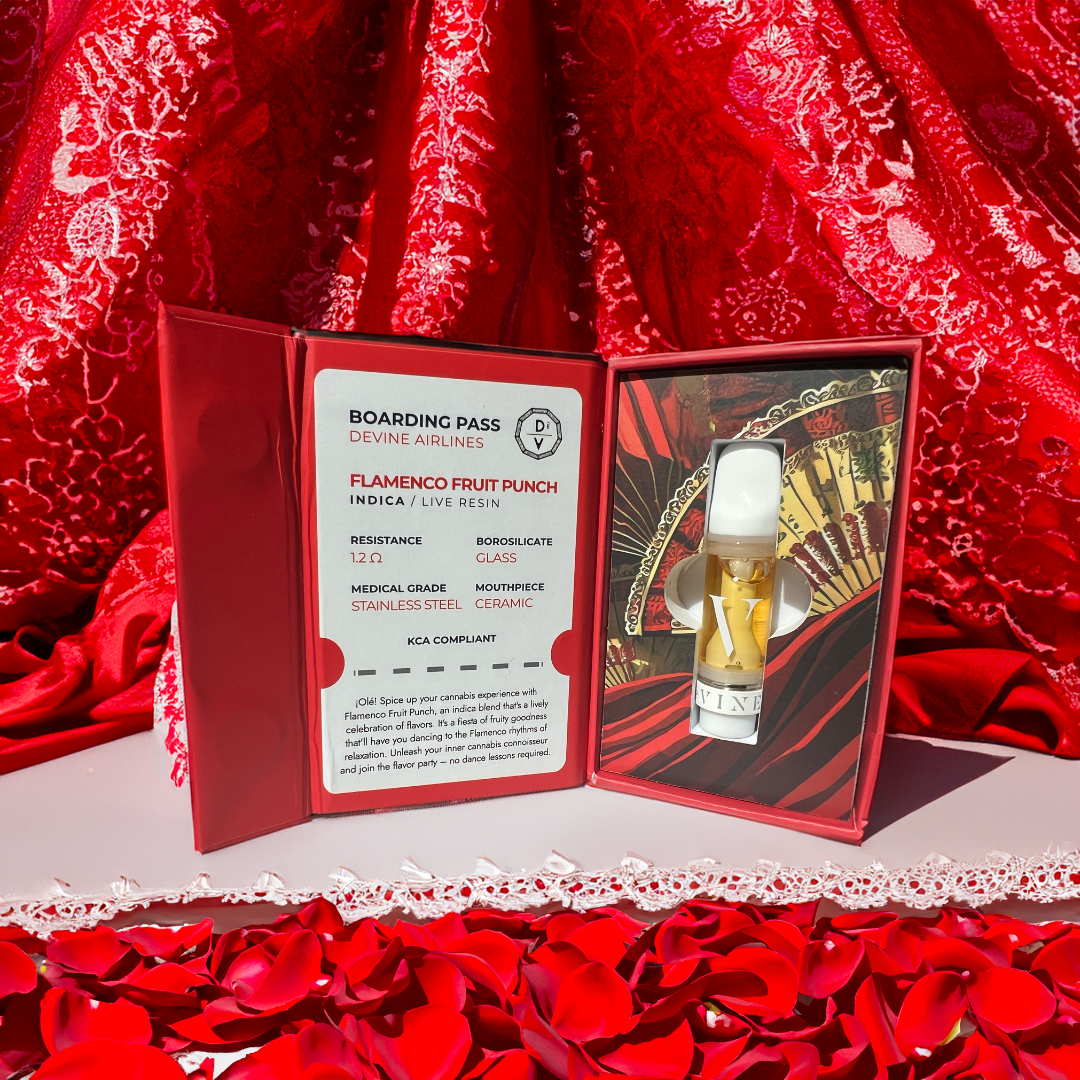 A red box with a boarding pass labeled Flamenco Fruit Punch sits beside the DeVINE Destinations Live Resin THC Cartridge by DeVINE Wellness, displayed on rose petals with a Spanish fan and red lace—perfect for travel-inspired vaping.
